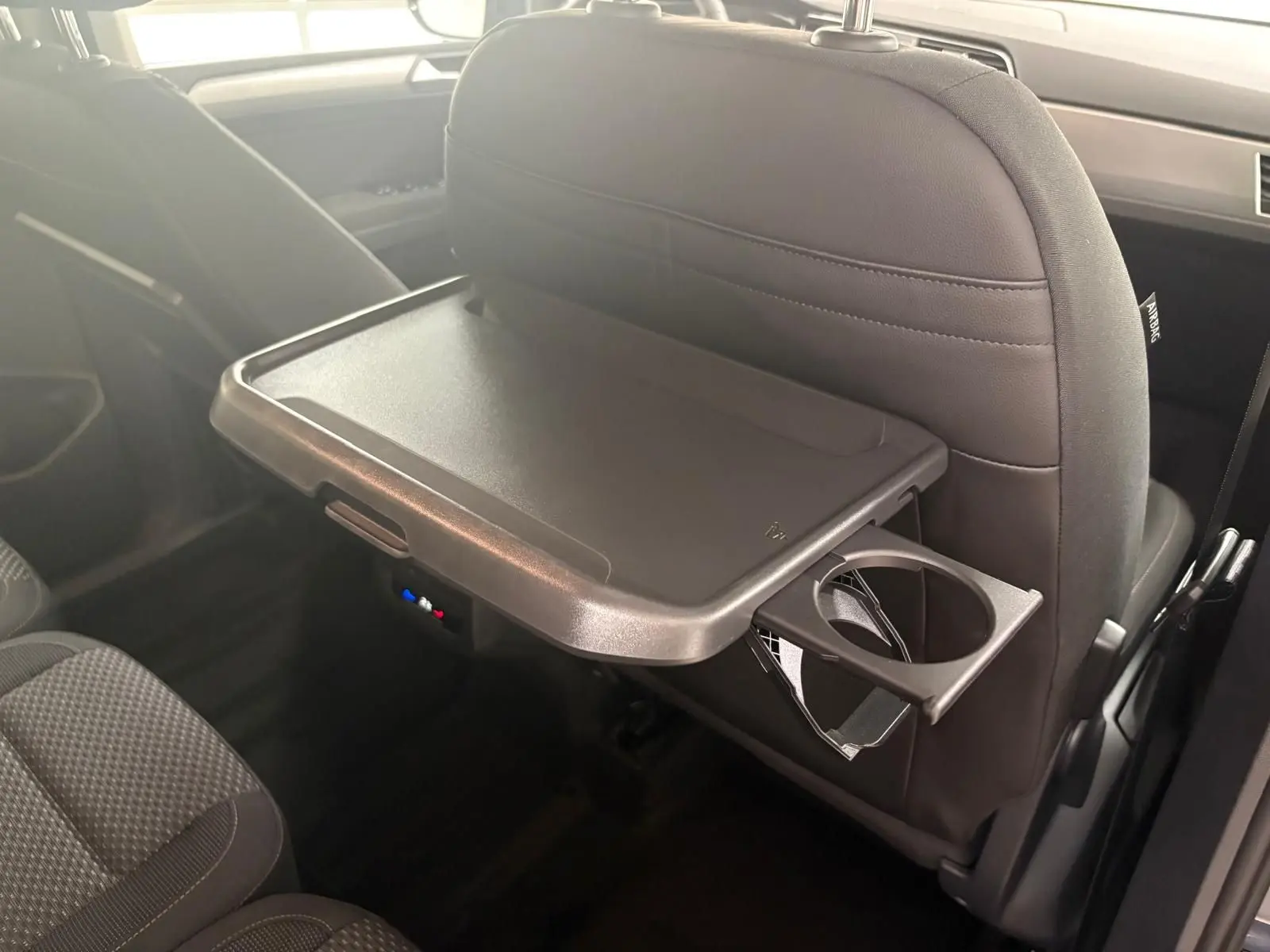 Tablette rabattable avec porte-gobelet fixée au dossier avant dans l'habitacle du Volkswagen Touran gris dauphin 2025.