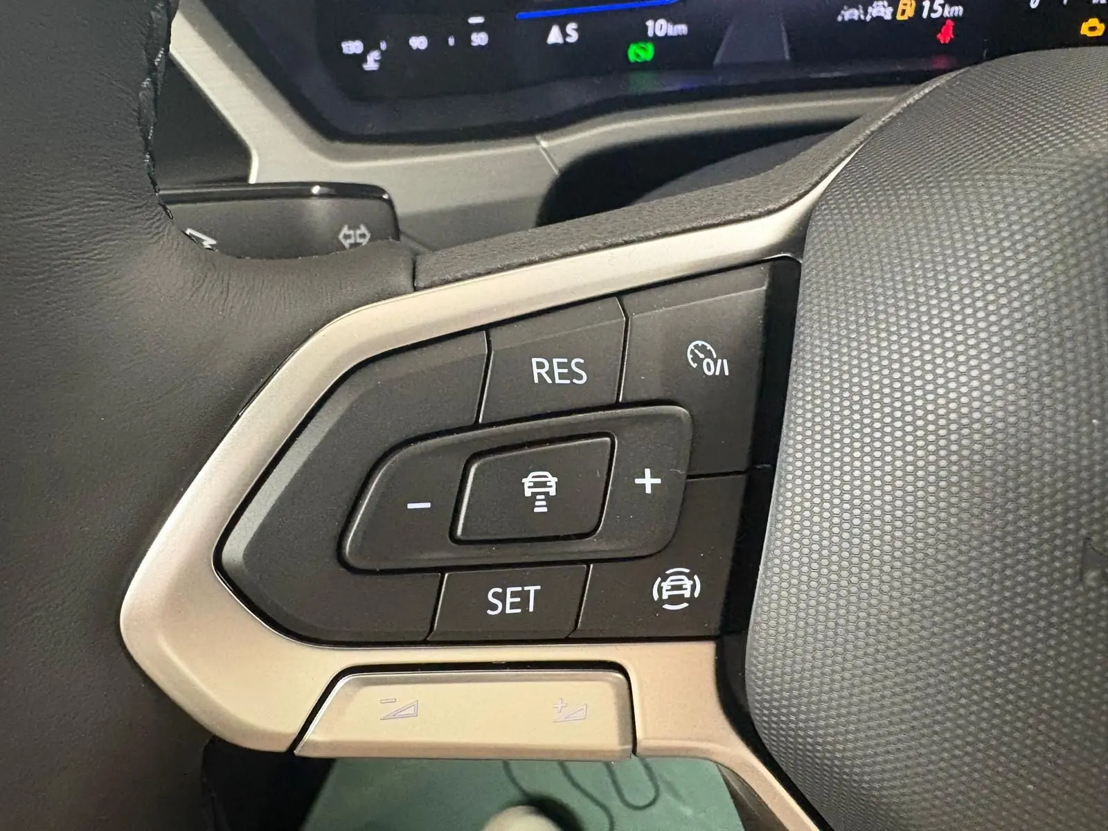 Gros plan sur les commandes au volant gauche du Volkswagen Touran gris dauphin, avec régulateur de vitesse adaptatif.