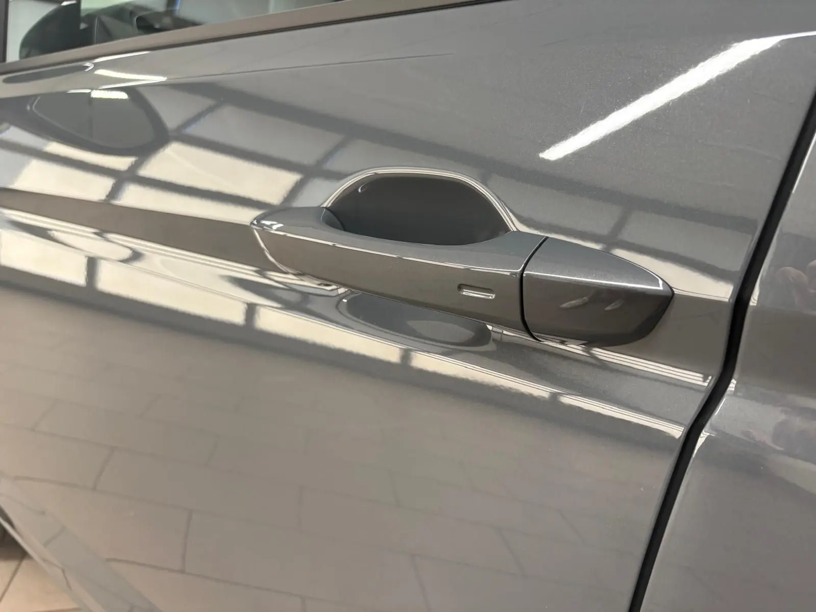 Poignée de porte côté gauche gris dauphin du Volkswagen Touran 2025, finition VW Edition, reflet intérieur lumineux.