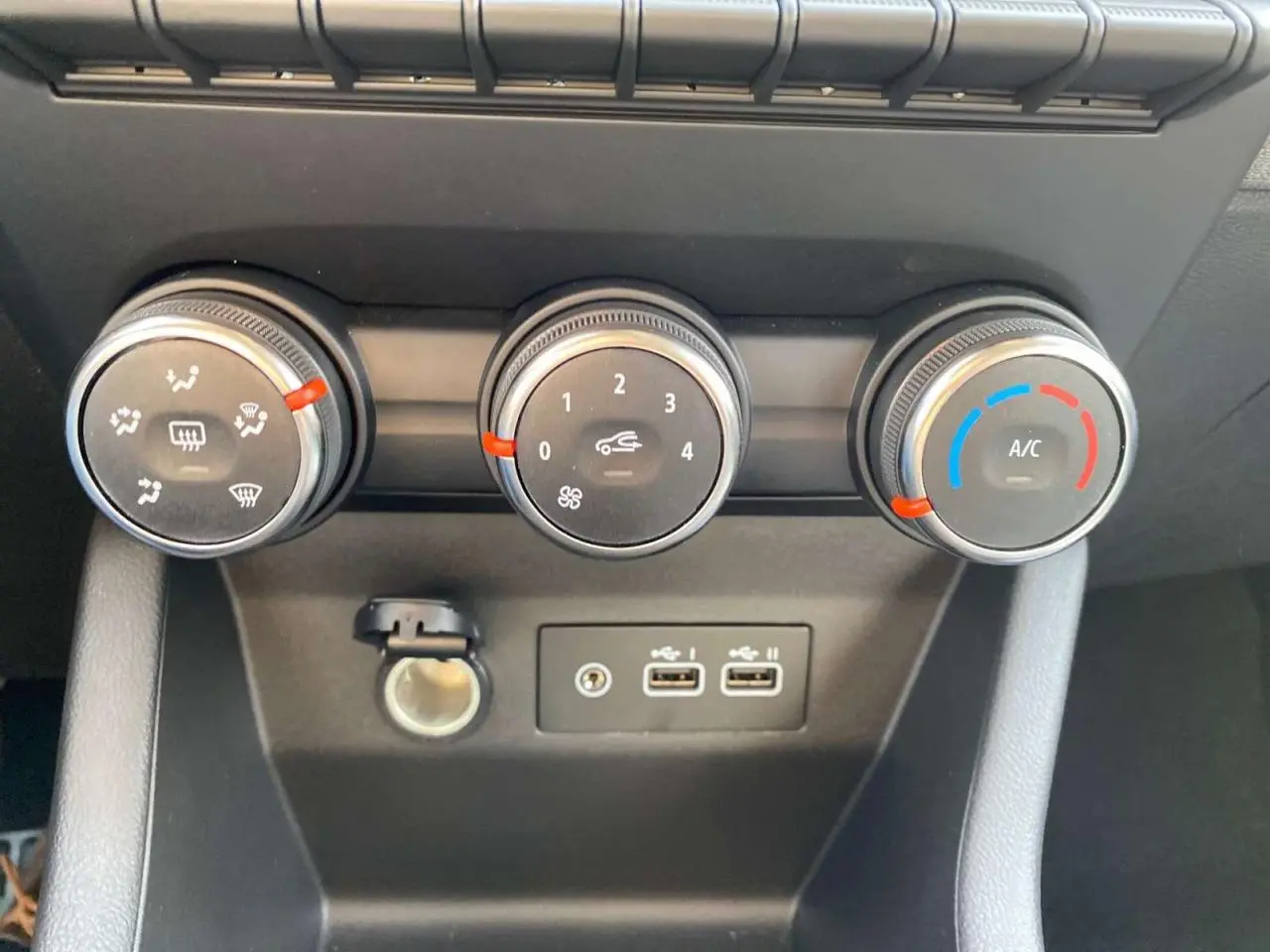 Gros plan sur les commandes de climatisation manuelle noire avec anneaux chromés et ports USB de la Renault Clio 1.5 Blue dCi noire.