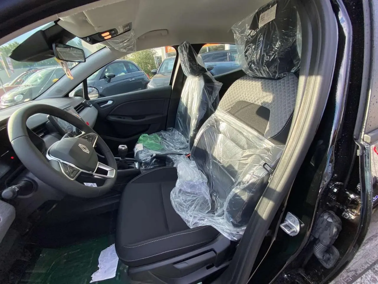 Vue intérieure côté conducteur de la Renault Clio 1.5 Blue dCi noire, sièges protégés par film plastique, volant multifonction visible.