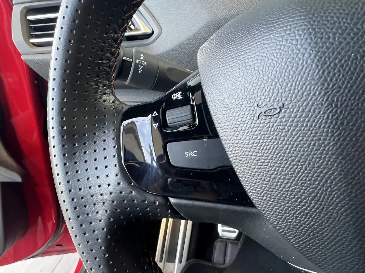 Gros plan sur le volant cuir perforé de la Peugeot 308 GT Line rouge, avec commandes audio intégrées.