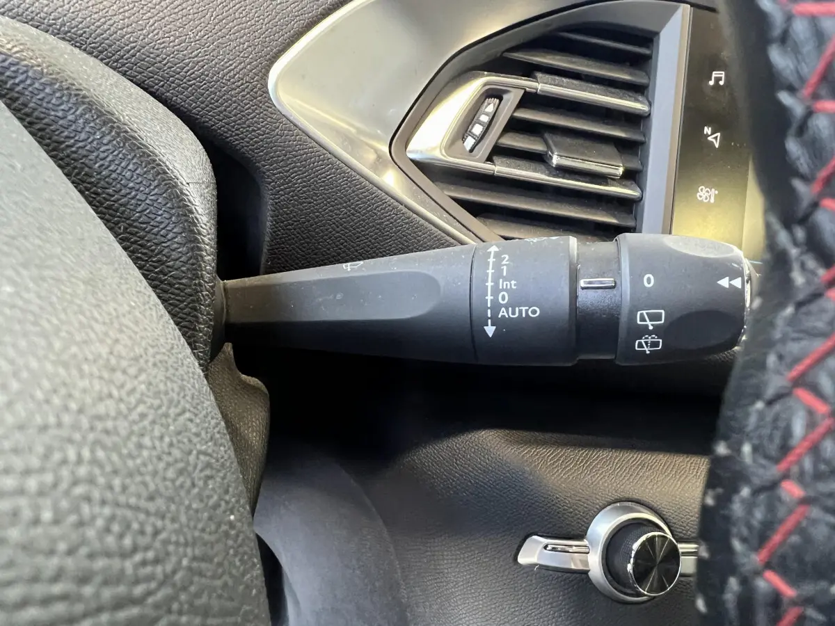 Gros plan sur la commande d’essuie-glace à gauche du volant cuir avec surpiqûres rouges dans un Peugeot 308 rouge.