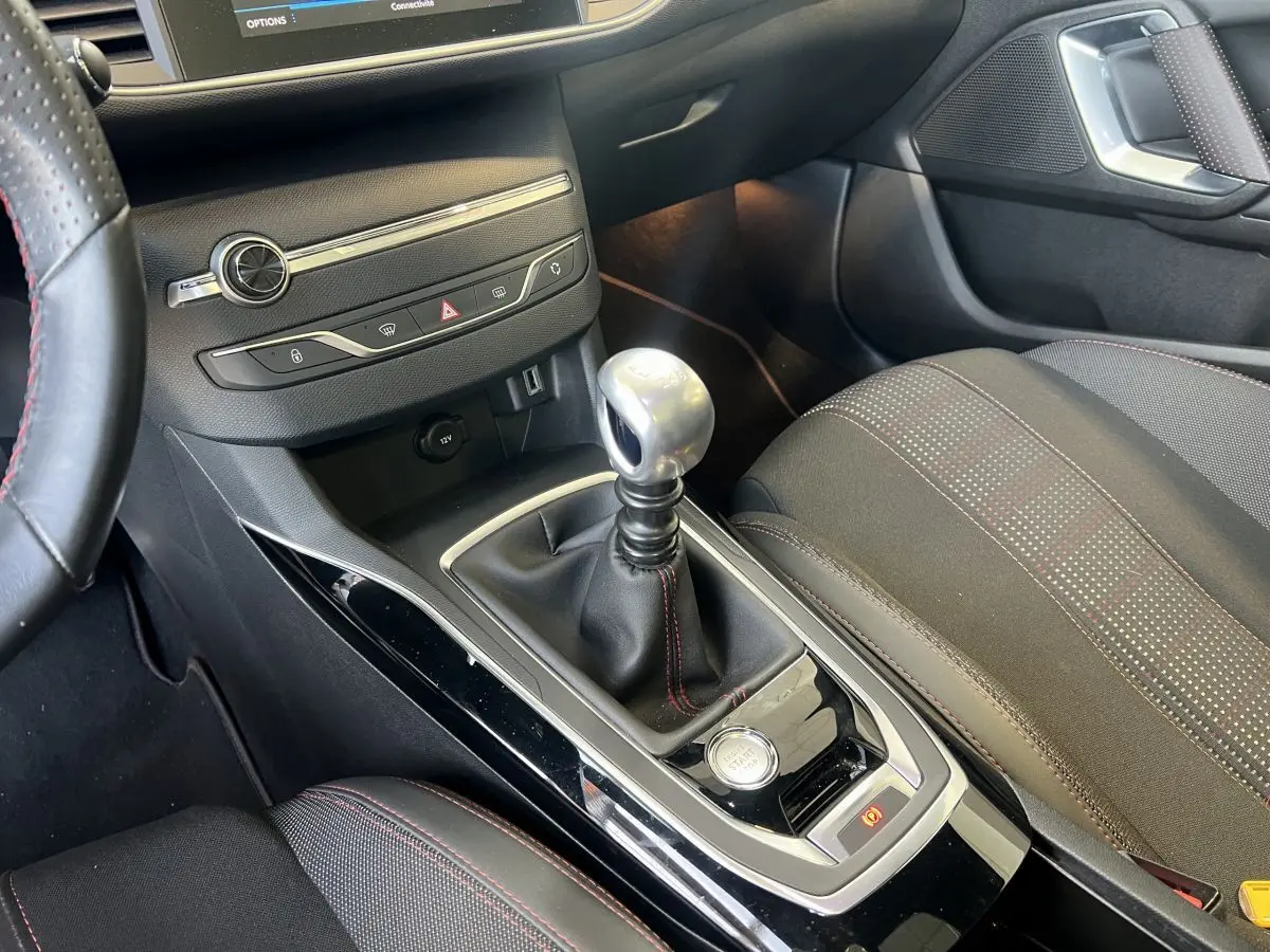 Vue rapprochée de la console centrale d'une Peugeot 308 GT Line rouge avec levier de vitesse manuel et bouton démarrage.