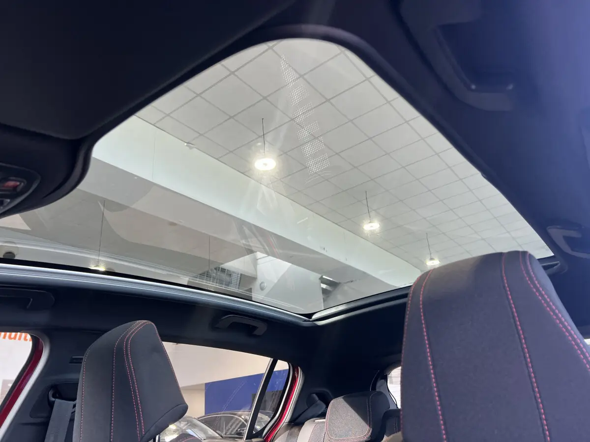 Vue intérieure du toit panoramique et des sièges avant avec surpiqûres rouges d'une Peugeot 308 rouge Puretech 130 S&S GT Line 2019