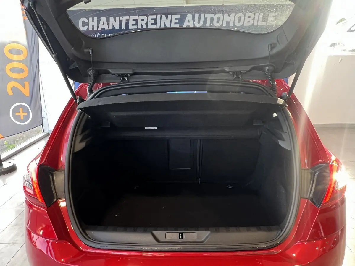 Coffre ouvert d'une Peugeot 308 Puretech 130 S&S GT Line rouge vue de l'arrière en intérieur showroom.
