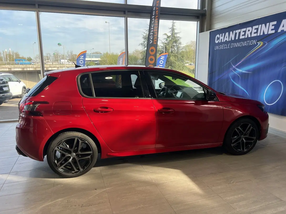 Profil latéral droit d'une Peugeot 308 Puretech 130 S&S GT Line rouge brillante avec jantes alliage noires en showroom.
