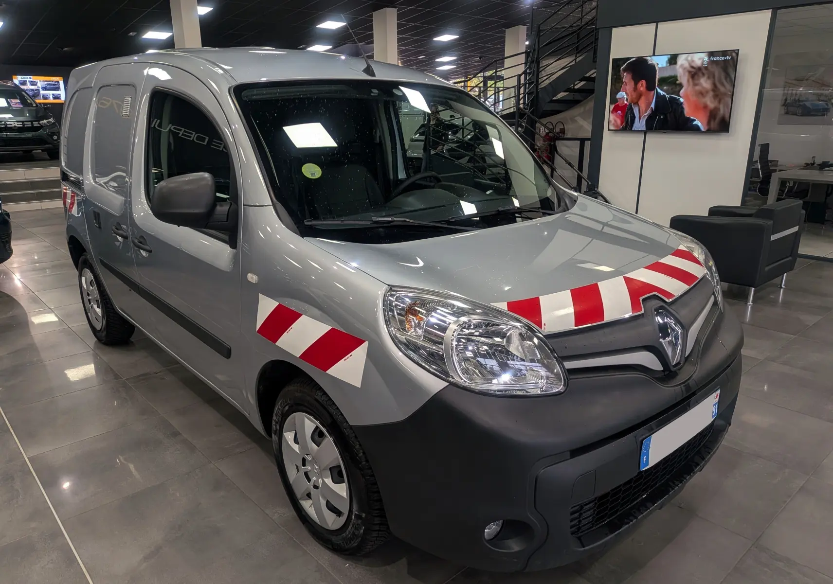 Vue 3/4 avant droit d'un Renault Kangoo Express gris Highland avec bandes rouges et blanches sur le capot et l'aile.