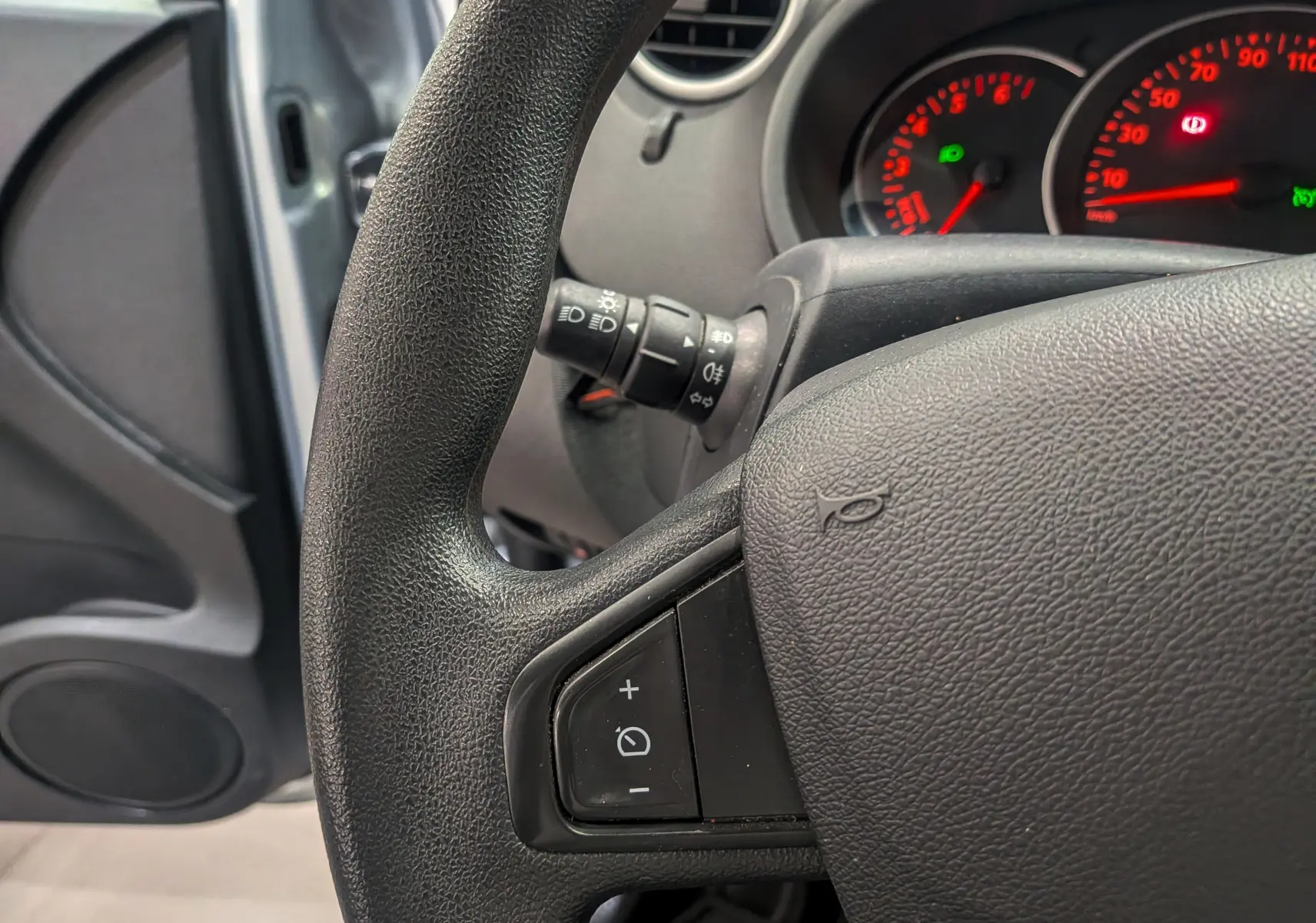 Gros plan sur le volant noir du Renault Kangoo Express 2021 avec commandes intégrées et tableau de bord éclairé en rouge.