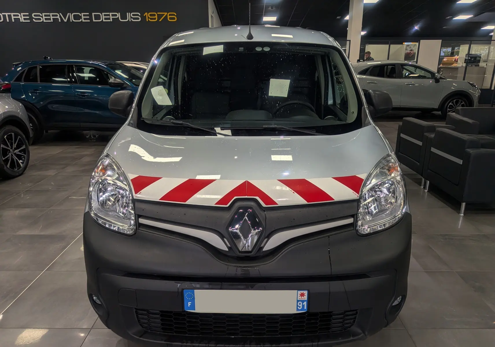 Vue frontale du Renault Kangoo Express gris Highland avec bandes rouges et blanches sur le capot, en intérieur showroom.