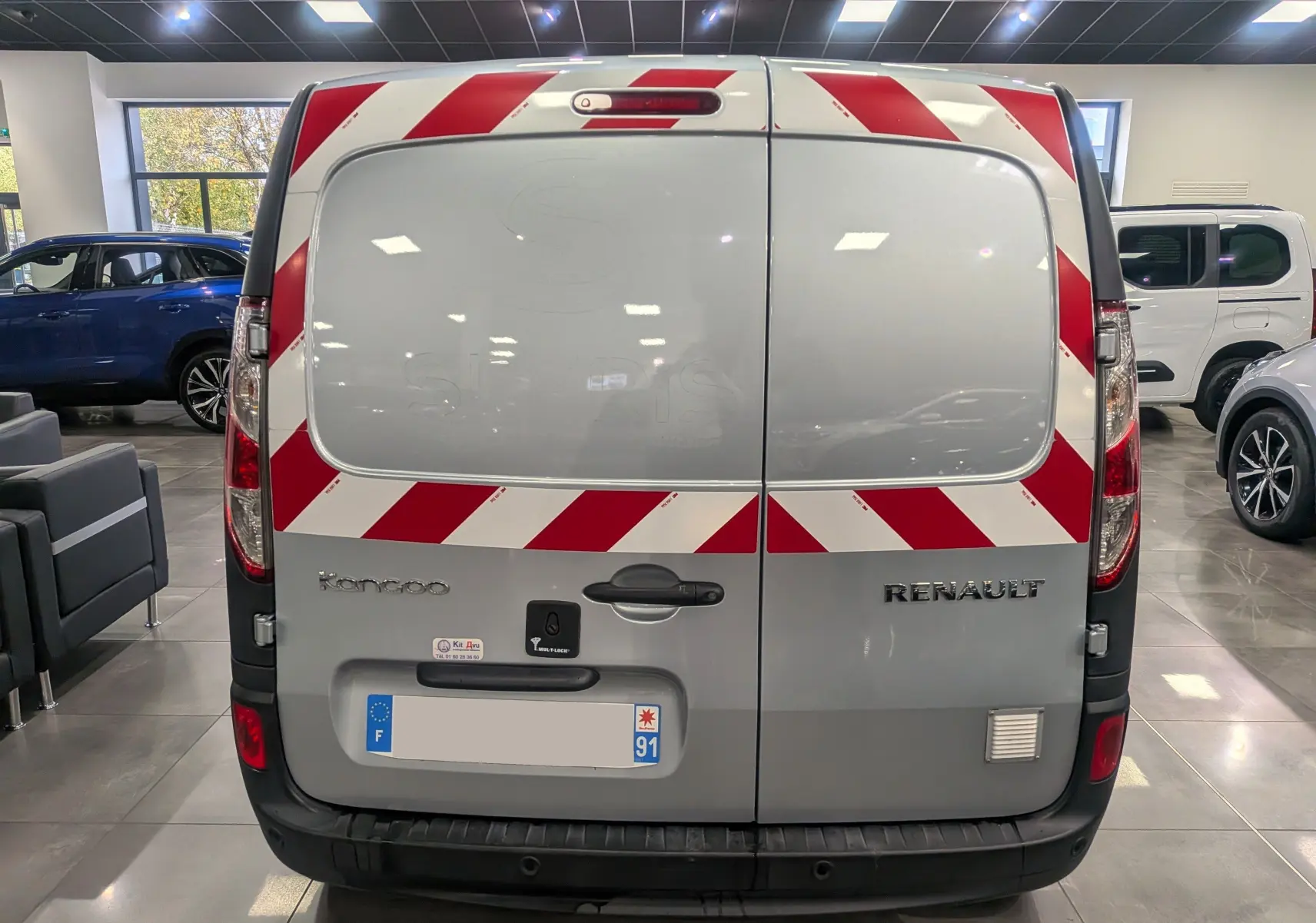 Vue arrière d'un Renault Kangoo Express gris Highland avec bandes rouges et blanches de signalisation sur les portes arrière.