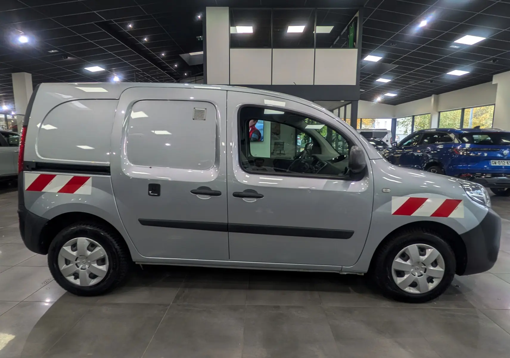 Profil gauche d'un Renault Kangoo Express gris Highland avec bandes réfléchissantes rouges et blanches sur les ailes avant et arrière.