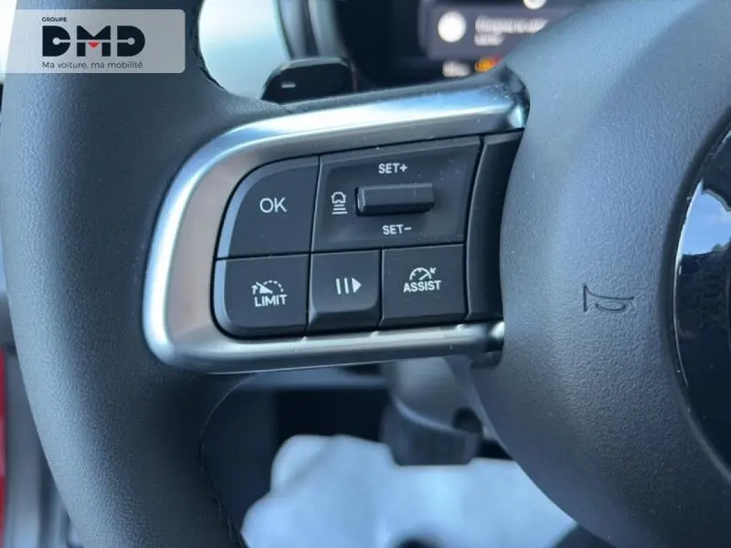 Gros plan sur les commandes multifonctions à gauche du volant d’une FIAT 600 rouge hybride, boutons de régulateur et limiteur de vitesse.