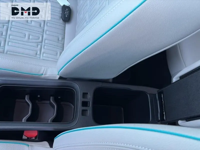 Vue rapprochée de l’accoudoir central blanc avec surpiqûres bleues et porte-gobelets du FIAT 600 hybride rouge.