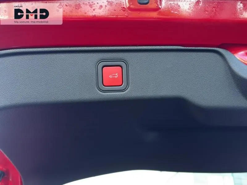 Bouton rouge d'ouverture électrique du coffre sur la partie intérieure du hayon d'une FIAT 600 rouge vue de dessous.