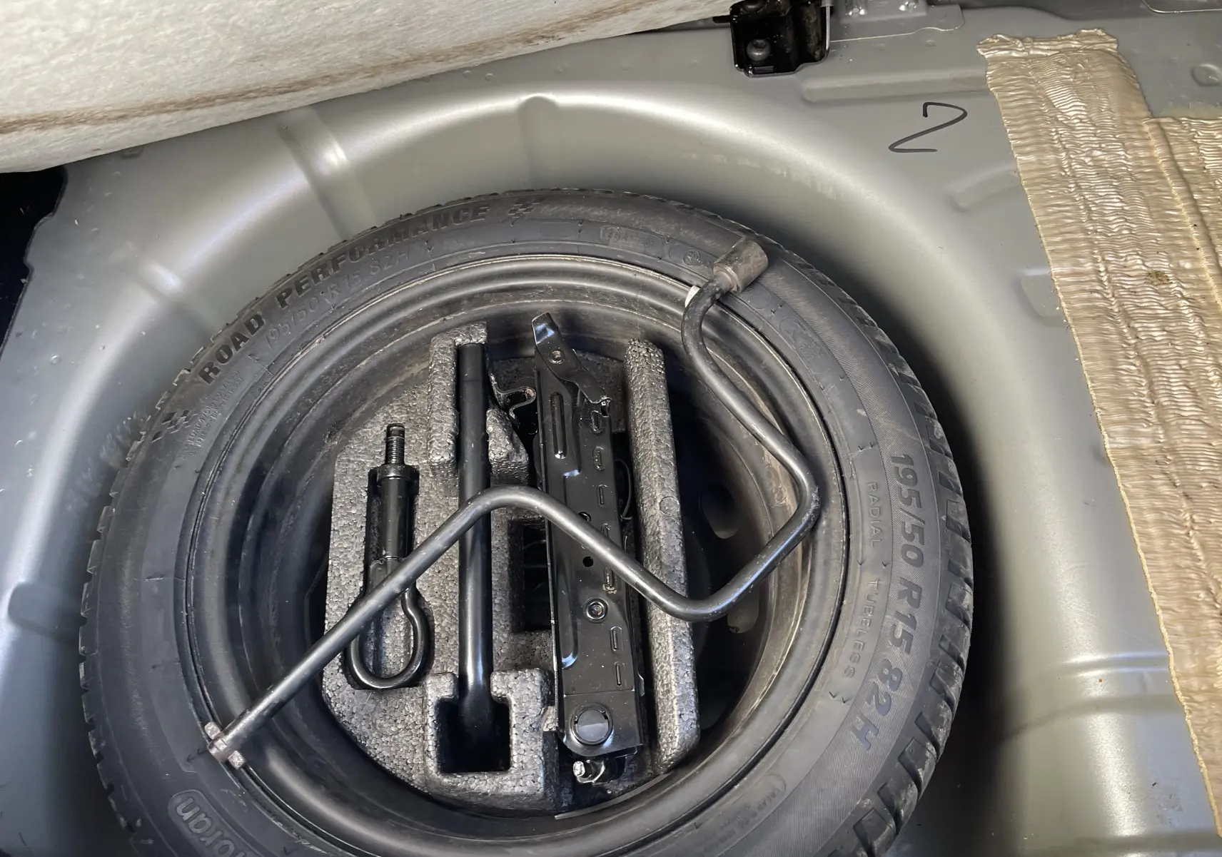 Vue en plongée sur la roue de secours noire et ses outils dans le coffre gris titane d'une Ford Fiesta 2014.