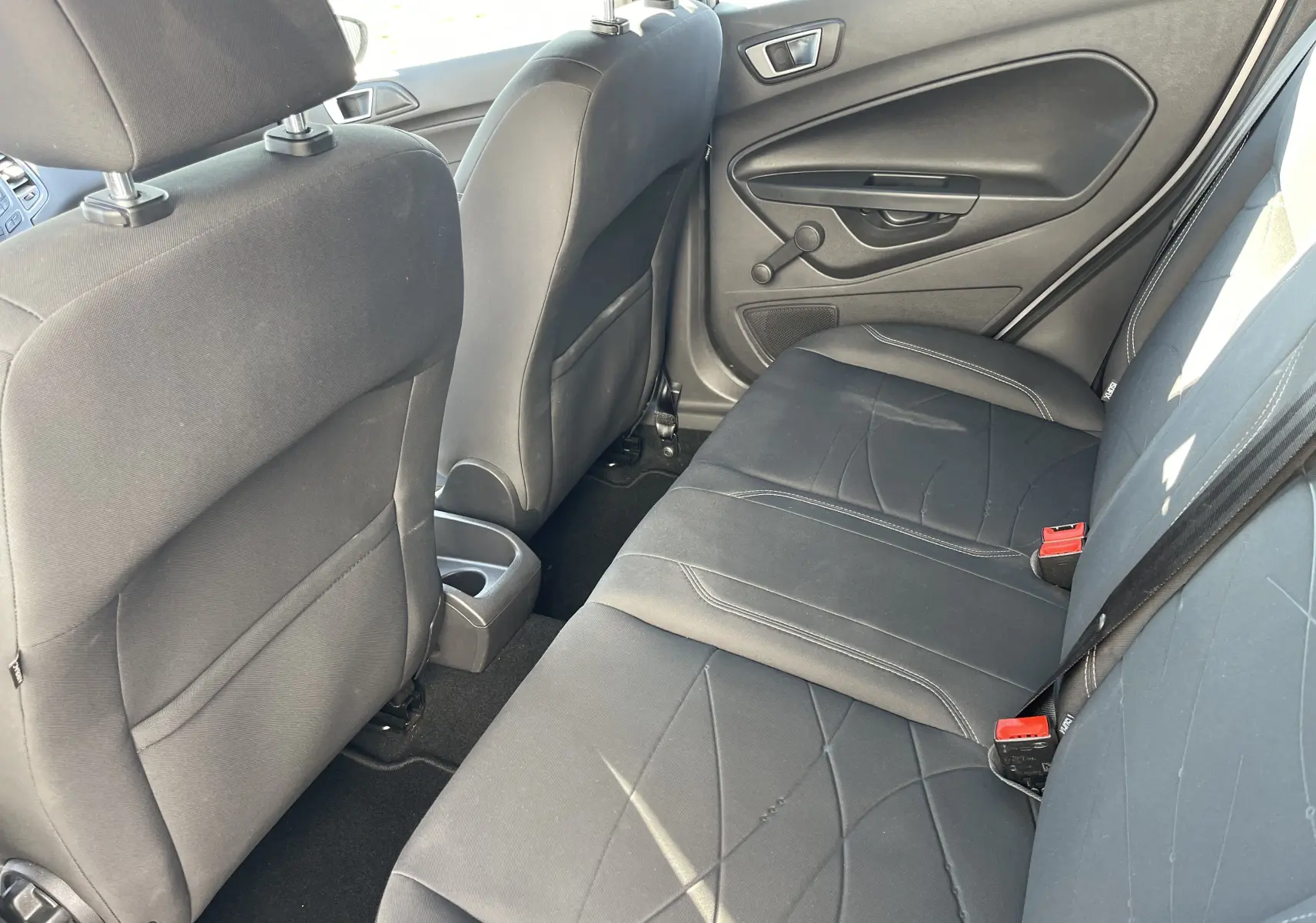 Vue intérieure arrière côté droit d'une Ford Fiesta 2014 gris titane, sièges noirs avec surpiqûres blanches et manivelle de vitre.