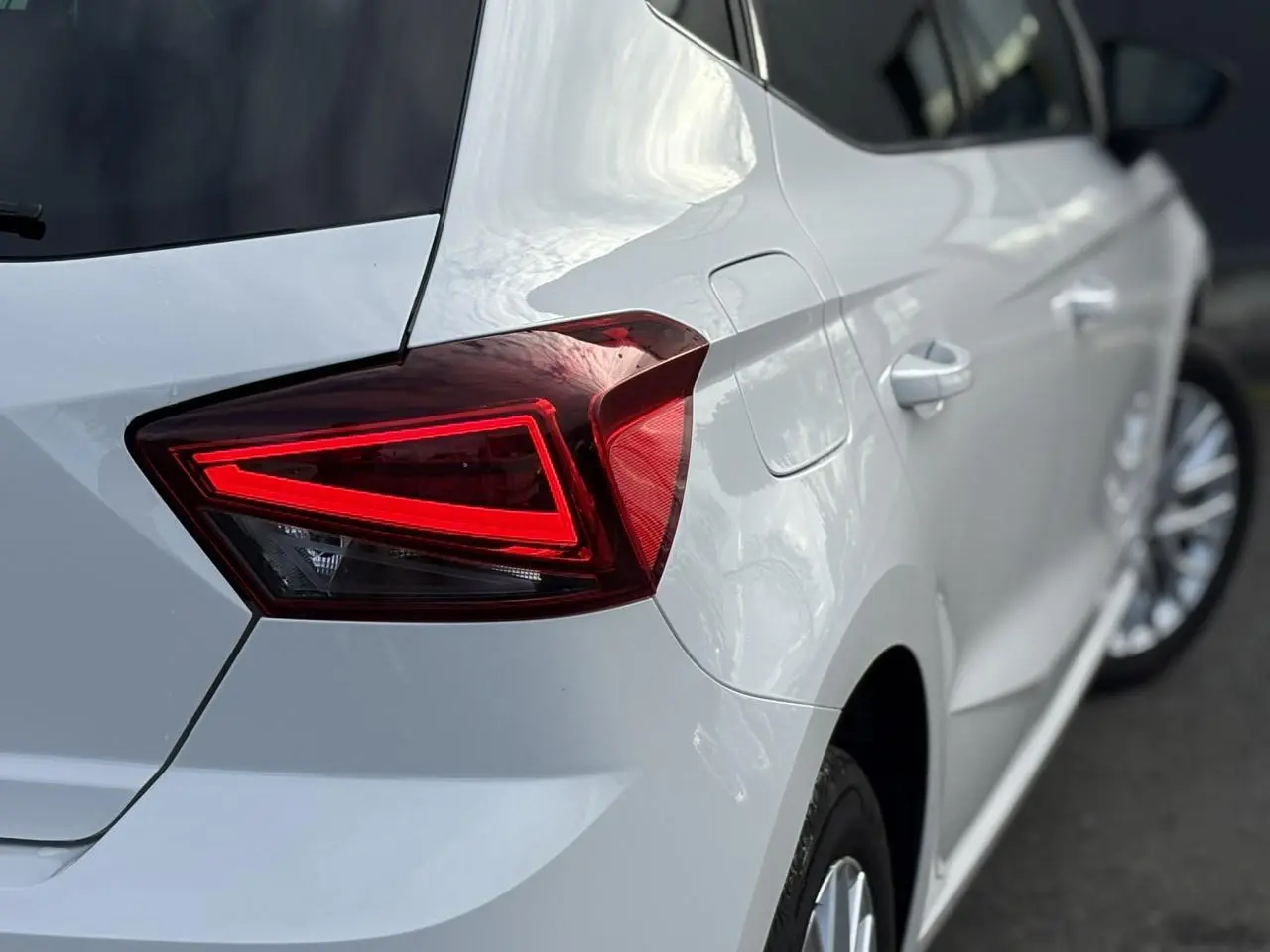 Gros plan sur le feu arrière droit rouge d'une SEAT Ibiza blanche, avec partie latérale et jante visible.