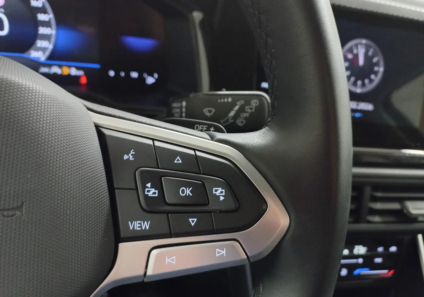 Gros plan sur les commandes au volant noir et argent du Volkswagen Taigo 2025, avec tableau de bord numérique en arrière-plan.