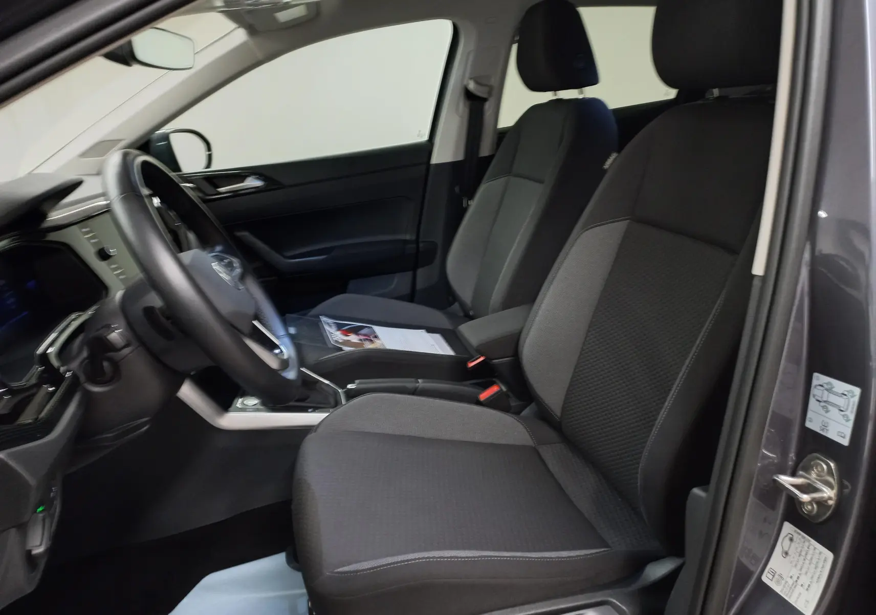 Vue intérieure côté conducteur du Volkswagen Taigo gris cendré 2025, sièges tissu noirs et tableau de bord moderne.