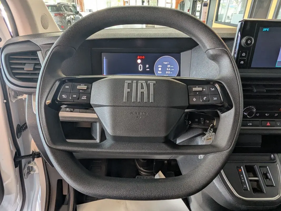 Vue rapprochée du volant noir FIAT du Scudo Fourgon blanc 2025, avec tableau de bord numérique et écran tactile central.