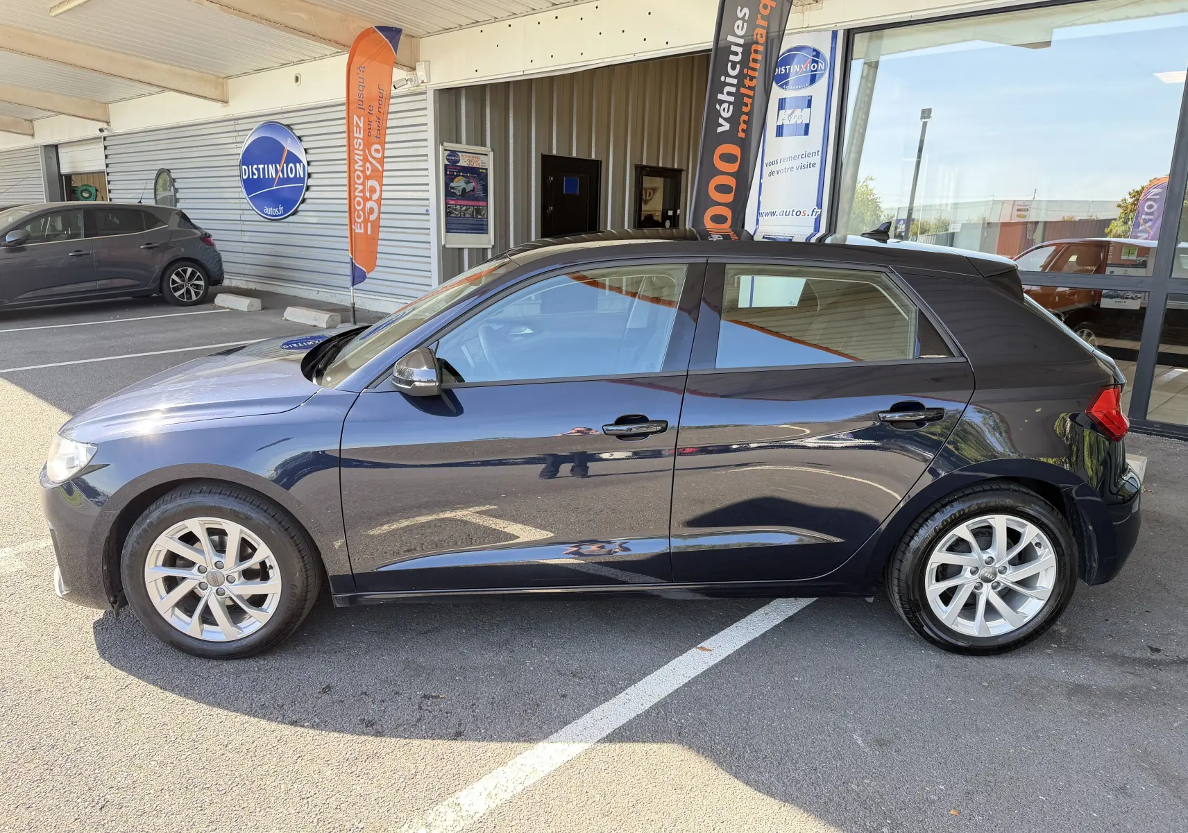 Audi A1 Sportback bleu firmament vue de profil côté gauche, garée devant un bâtiment commercial.