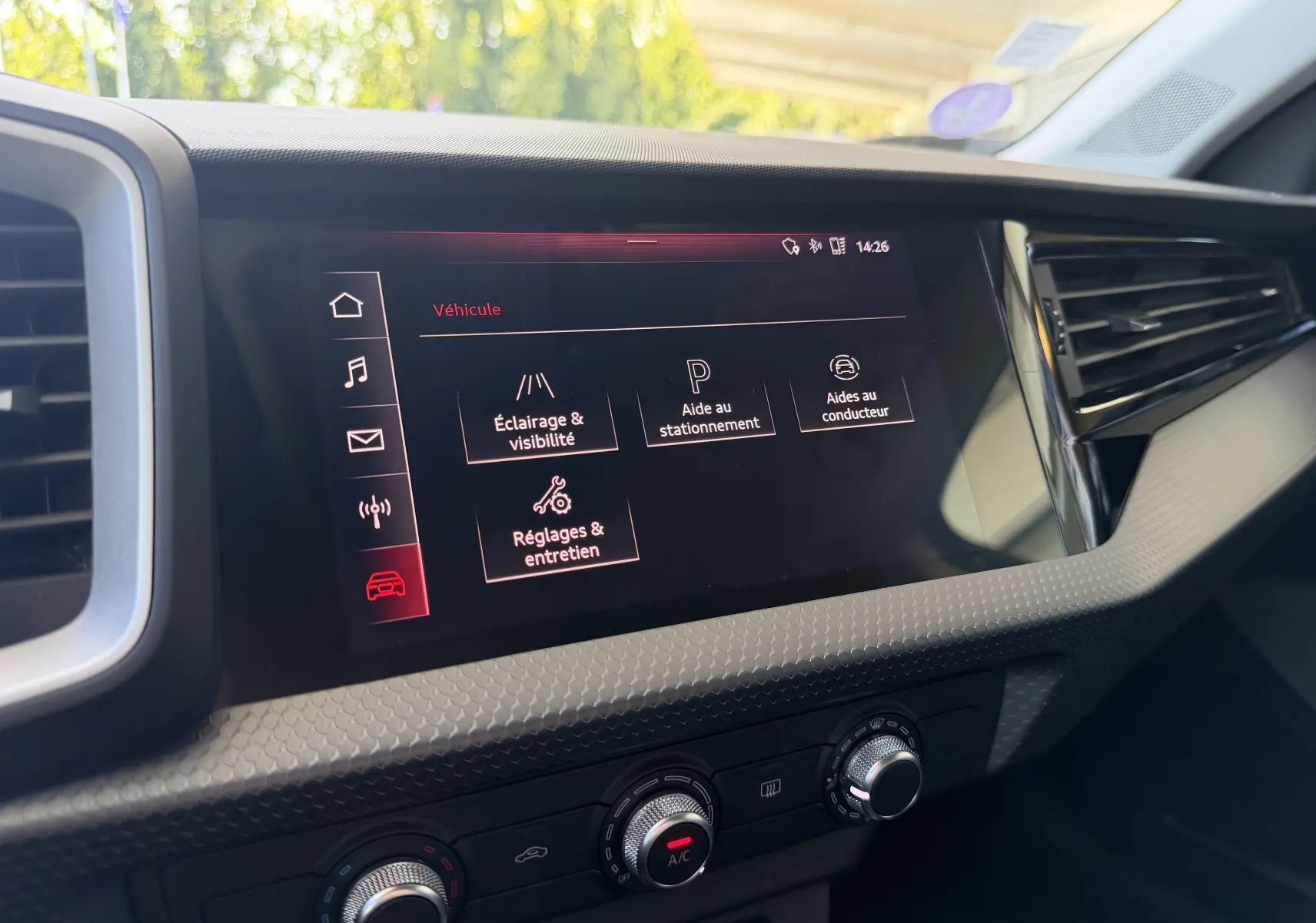 Écran tactile central de l’Audi A1 Sportback 2020 affichant les réglages véhicule, entouré de la console noire et des commandes de climatisation.