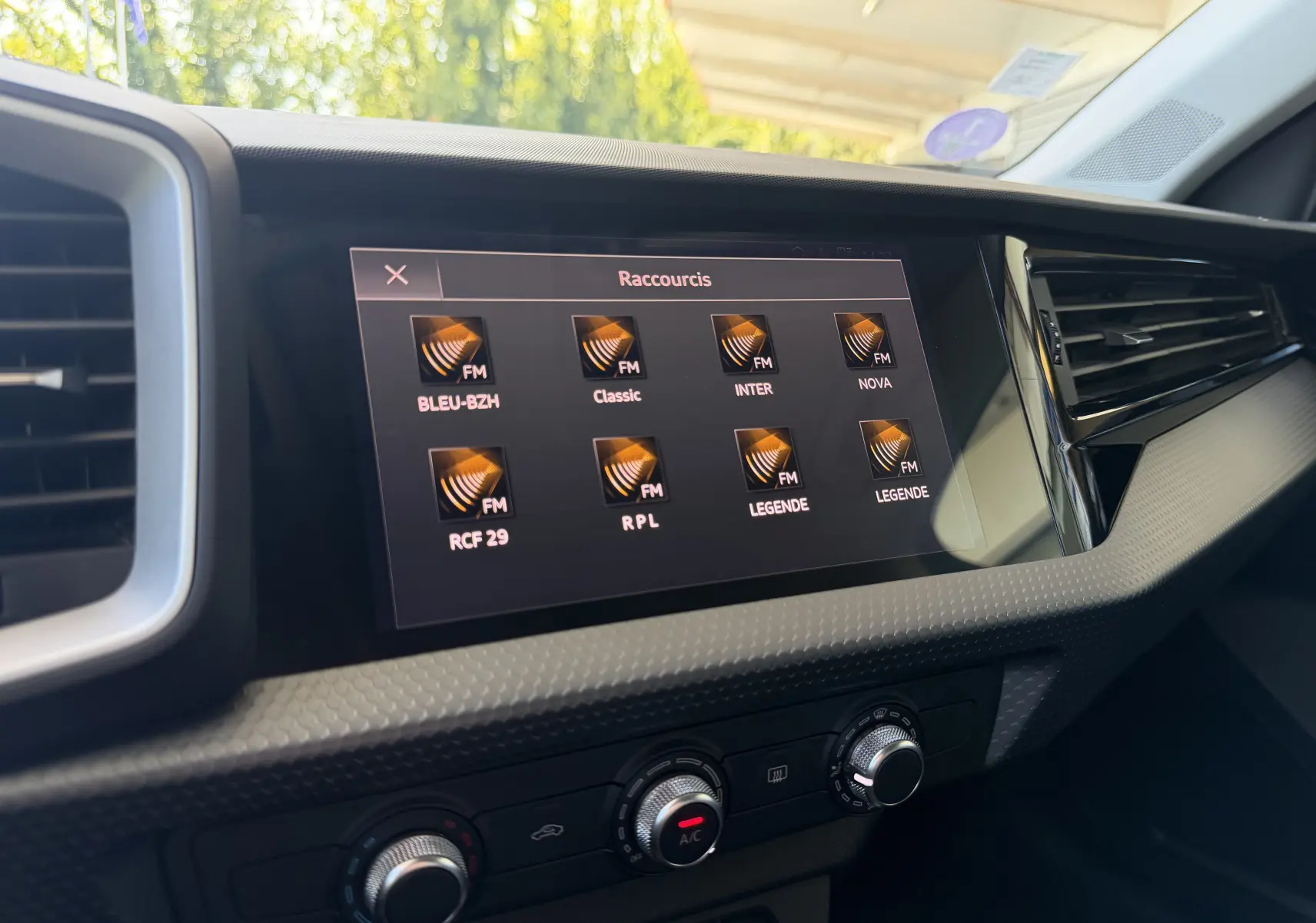 Écran tactile central de l’Audi A1 Sportback 2020 affichant les stations radio FM, avec commandes de climatisation en dessous.