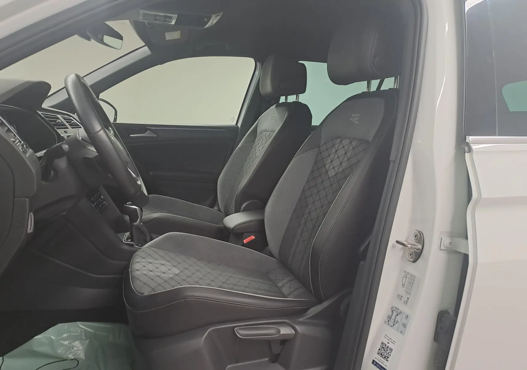 Intérieur côté gauche du Volkswagen Tiguan 1.4 eHybrid 245 DSG6 R-LINE 2023 avec sièges noirs en tissu et cuir, porte blanche ouverte.