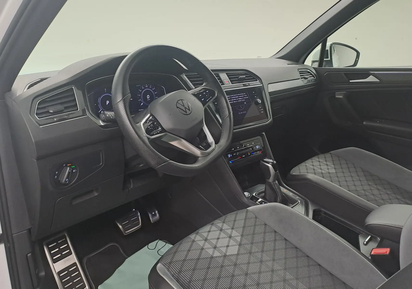 Intérieur du Volkswagen Tiguan 2023 hybride rechargeable vu côté conducteur, avec volant multifonction et sièges tissu noir à motifs.