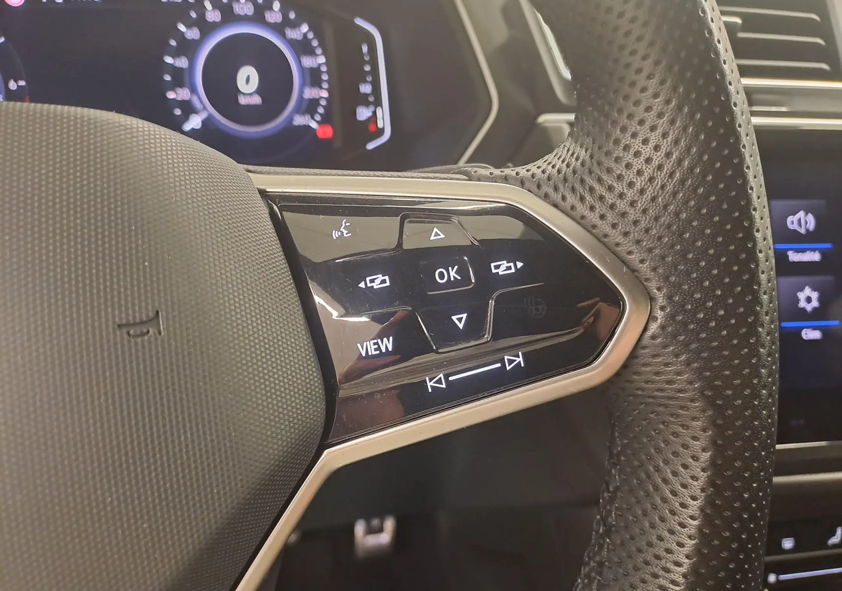 Gros plan sur la partie droite du volant perforé du Volkswagen Tiguan 1.4 eHybrid blanc avec commandes multifonctions et tableau de bord numérique.