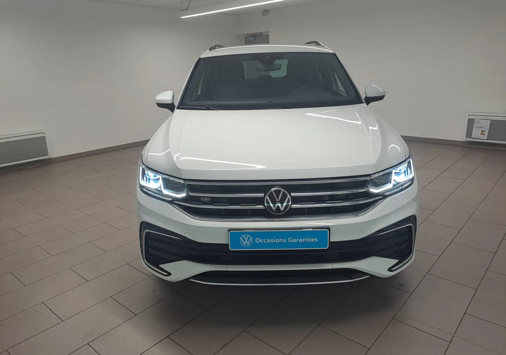 Vue frontale d'un Volkswagen Tiguan blanc pur 2023 avec phares LED allumés et finition R-Line dans un showroom.