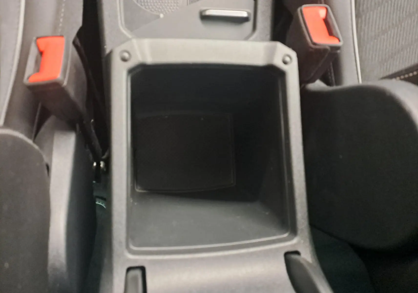 Gros plan sur le rangement central noir entre les sièges avant avec les ceintures rouges du Volkswagen Tiguan 1.4 eHybrid 2023.