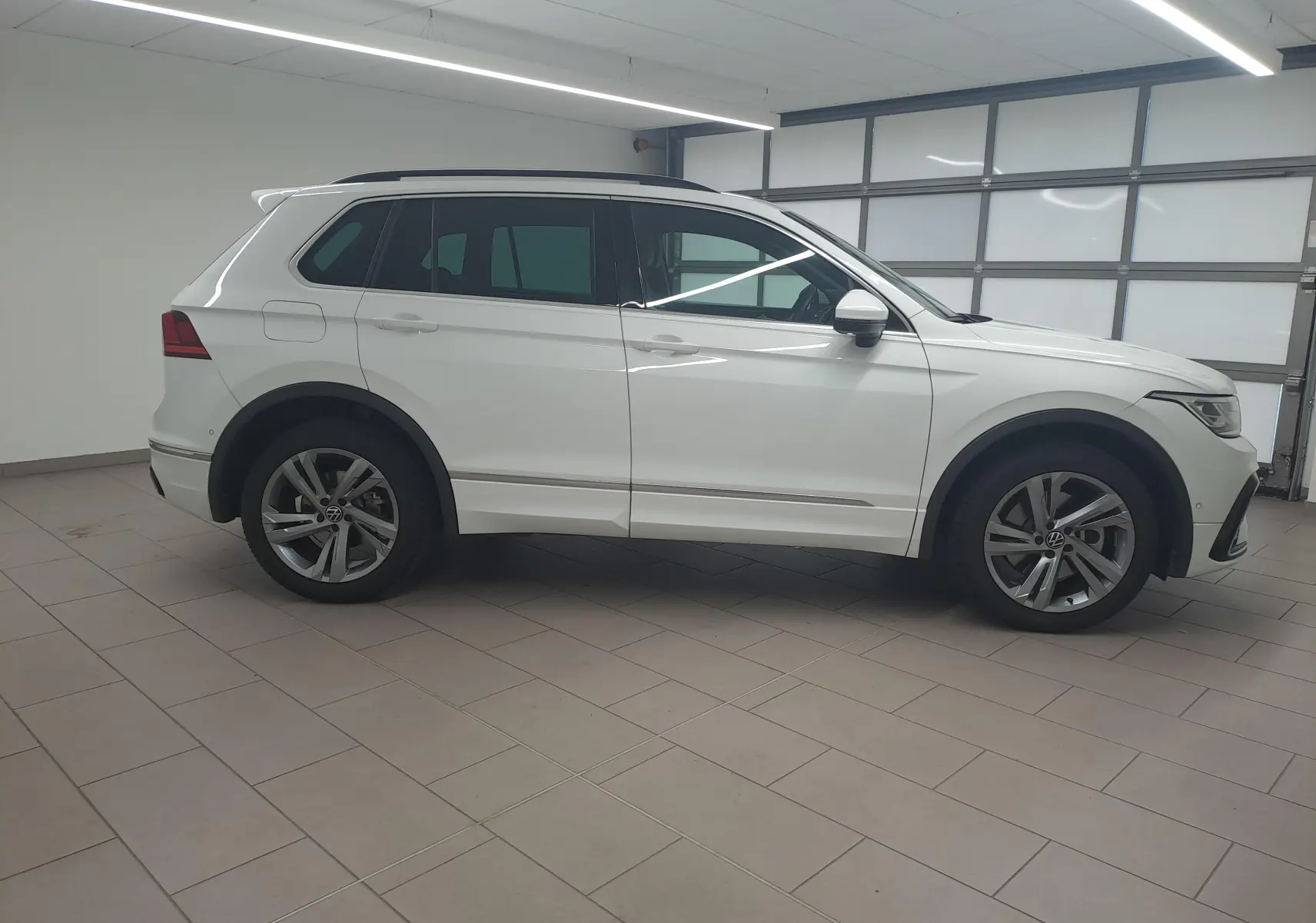 Vue de profil côté gauche d'un Volkswagen Tiguan 1.4 eHybrid blanc pur R-Line 2023 en intérieur.