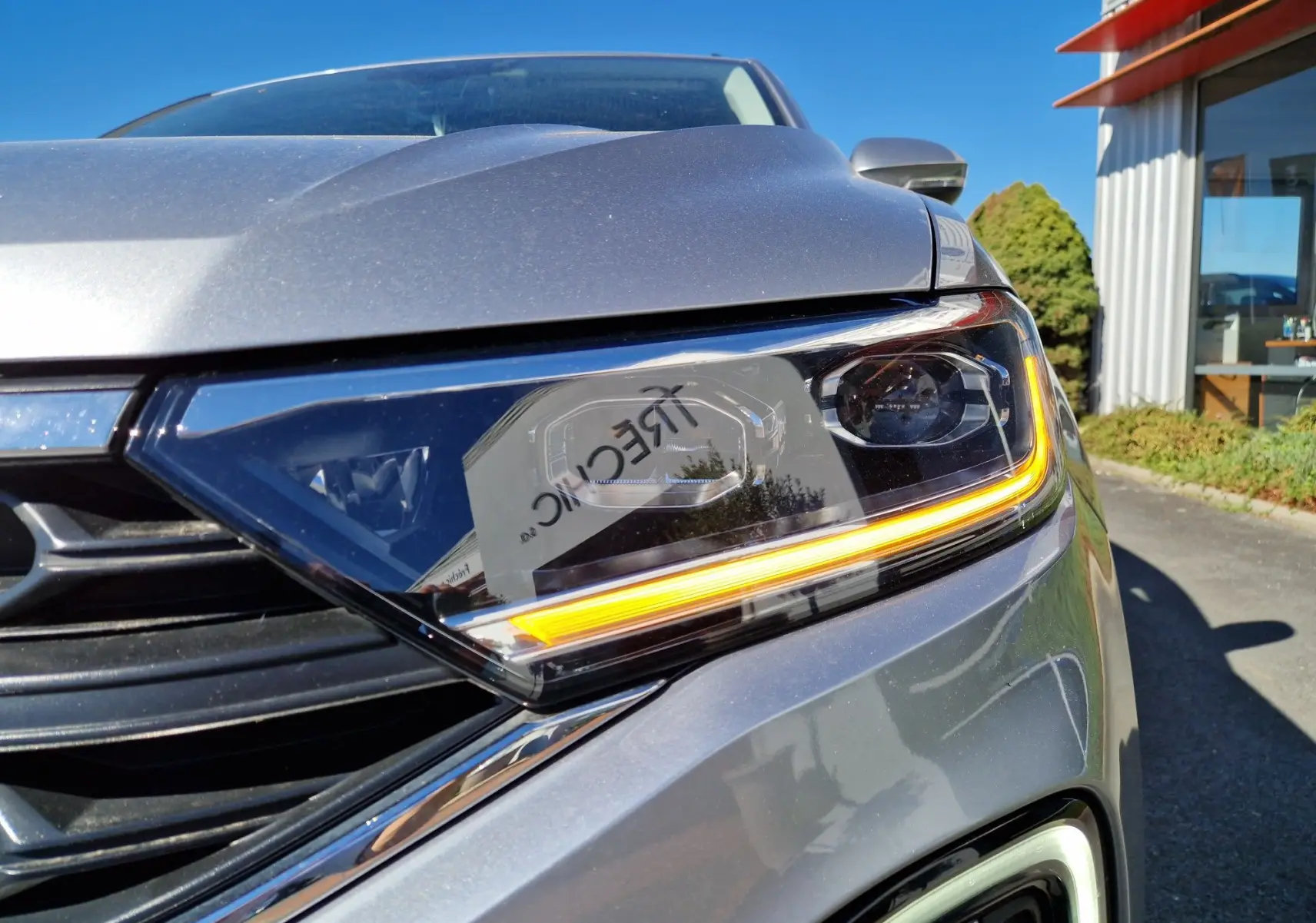 Gros plan sur le phare avant droit du Volkswagen T-Roc gris pyrite 2023 avec éclairage LED distinctif allumé.