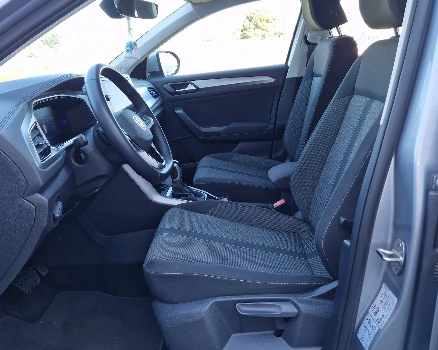 Intérieur côté conducteur d'un Volkswagen T-Roc gris pyrite 2023, sièges tissu noirs et tableau de bord moderne.