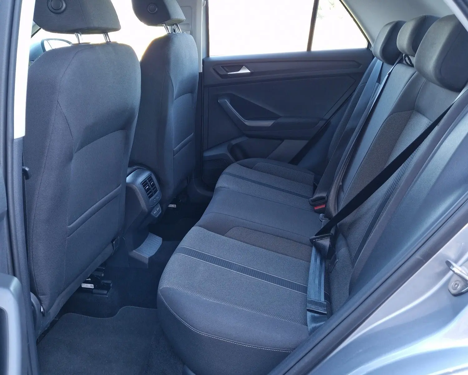 Vue côté gauche de l'habitacle arrière du Volkswagen T-Roc gris pyrite 2023 avec sièges tissu noirs et ceinture attachée.