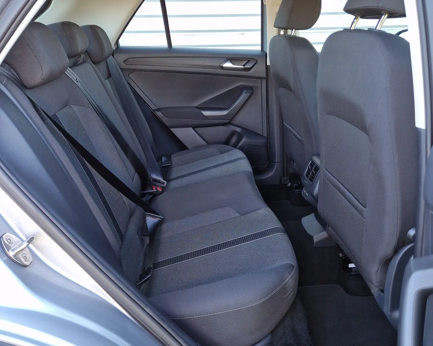 Vue intérieure côté gauche des sièges arrière en tissu gris du Volkswagen T-Roc gris pyrite 2023, avec ceinture de sécurité attachée.