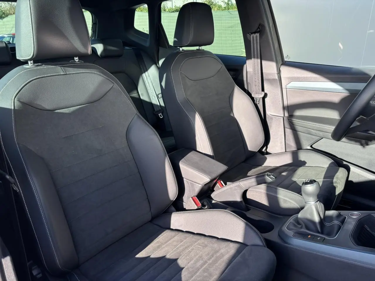 Vue intérieure côté conducteur et passager avant du SEAT Arona 2025, sièges en cuir noir avec surpiqûres blanches et levier de vitesses manuel.