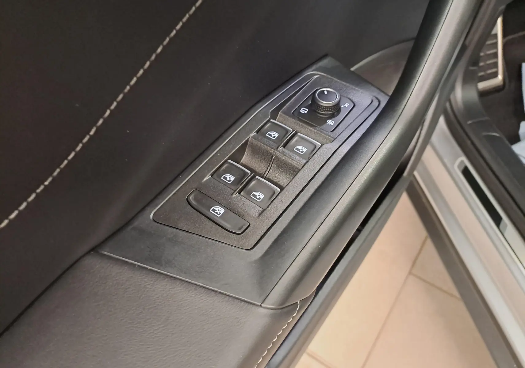 Gros plan sur les commandes des vitres et rétroviseurs sur la porte côté conducteur du Volkswagen T-Roc gris Pyrite 2025.