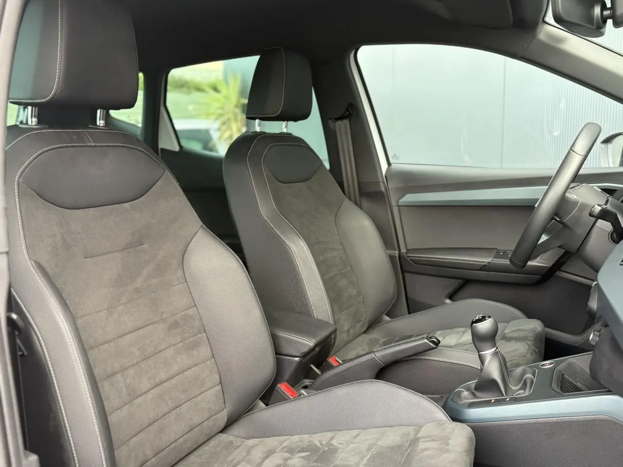 Intérieur du SEAT Arona 2025 montrant les sièges avant en tissu gris et la boîte manuelle côté droit.
