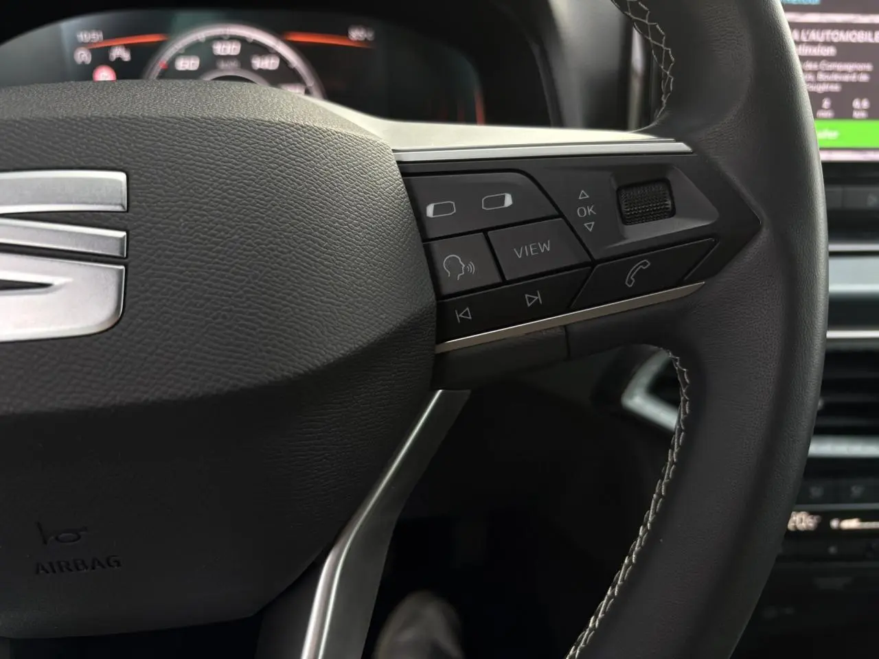 Gros plan sur le volant cuir multifonction du SEAT Arona TSI 115 Xpérience, avec commandes intégrées et logo SEAT visible.