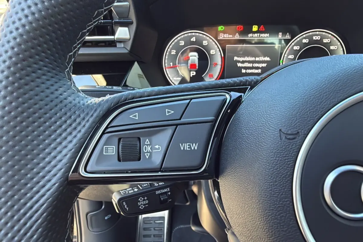 Gros plan sur les commandes gauche du volant cuir perforé de l'Audi A3 TFSI 150 Hybrid S-Line 2025.