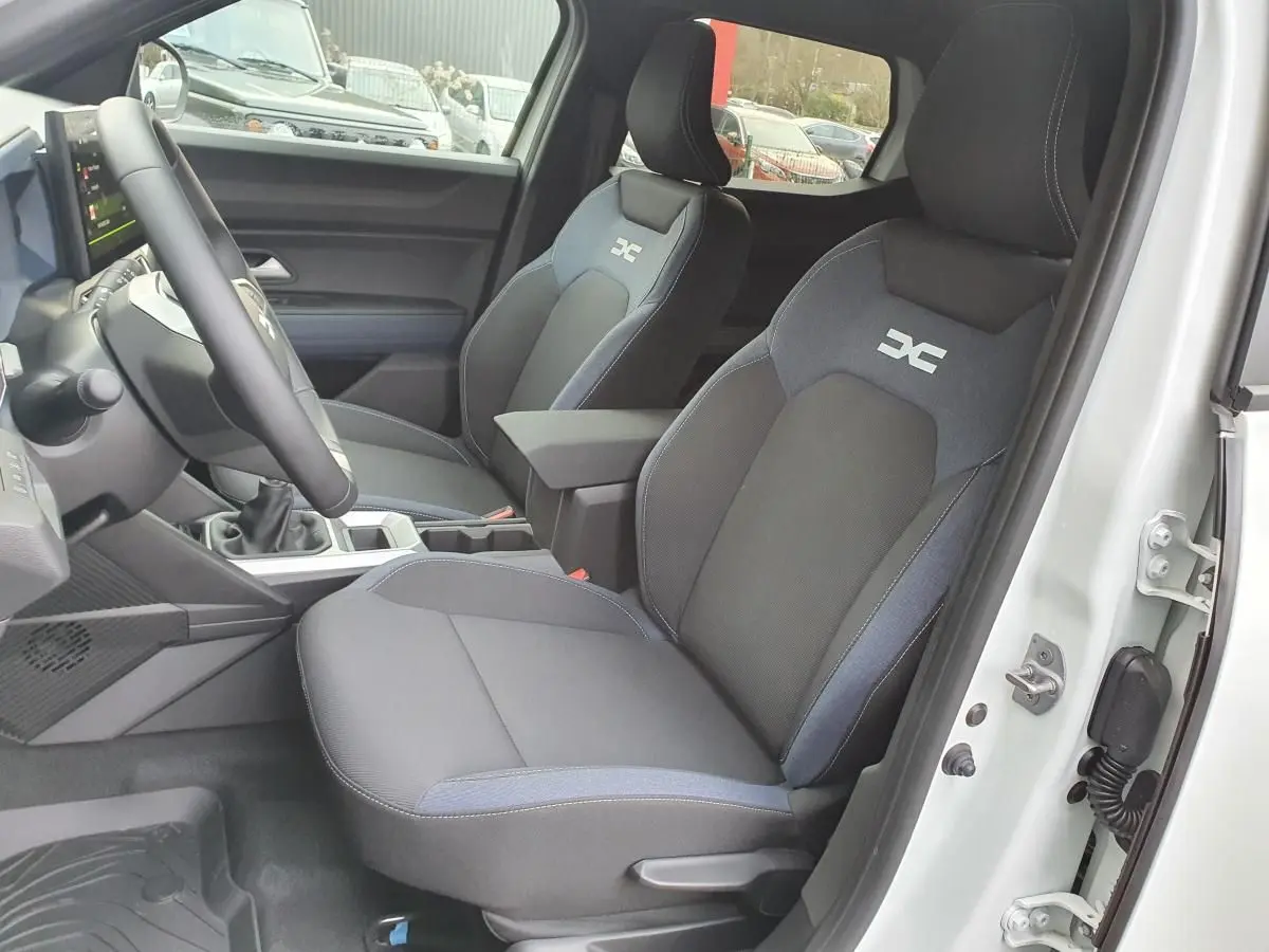 Vue intérieure côté conducteur du Dacia Duster blanc glacier 2025, sièges tissu avec logo distinctif DC brodé.
