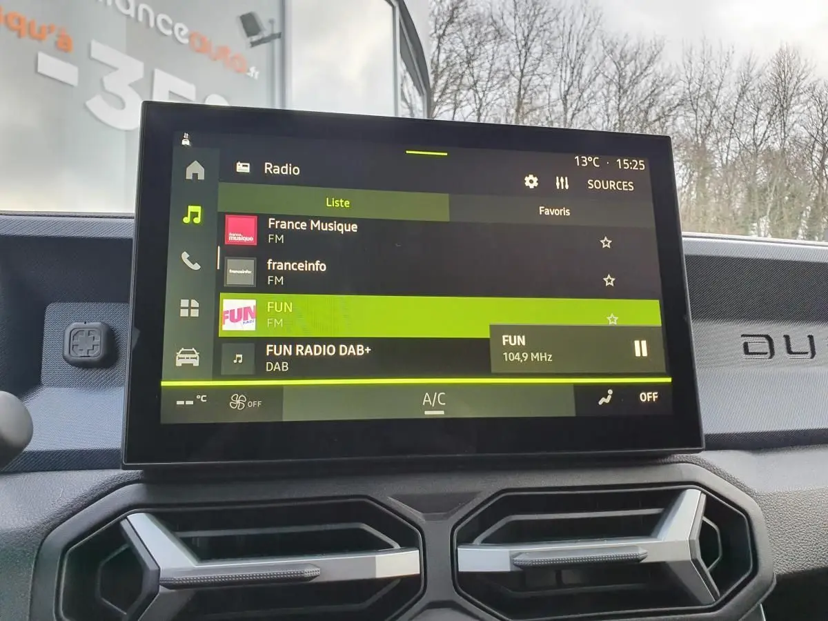 Vue intérieure centrée sur l'écran tactile du tableau de bord du Dacia Duster 2025, affichant la radio FM.