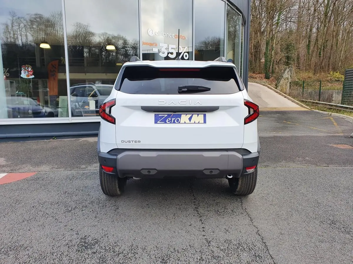 Vue arrière d'un Dacia Duster blanc glacier 2025 avec feux arrière en forme de C et pare-chocs gris foncé.