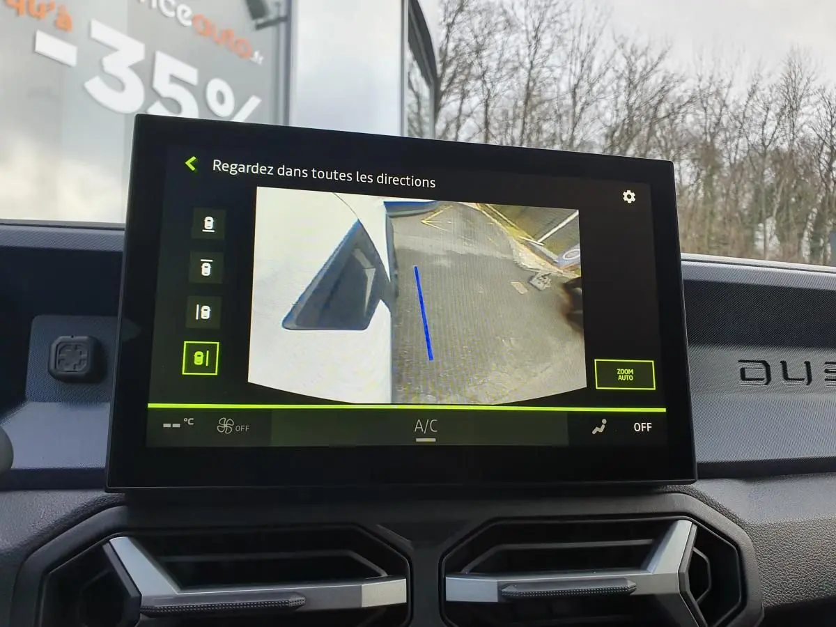 Écran central du Dacia Duster blanc glacier montrant la caméra multivues avec vue latérale droite en stationnement.
