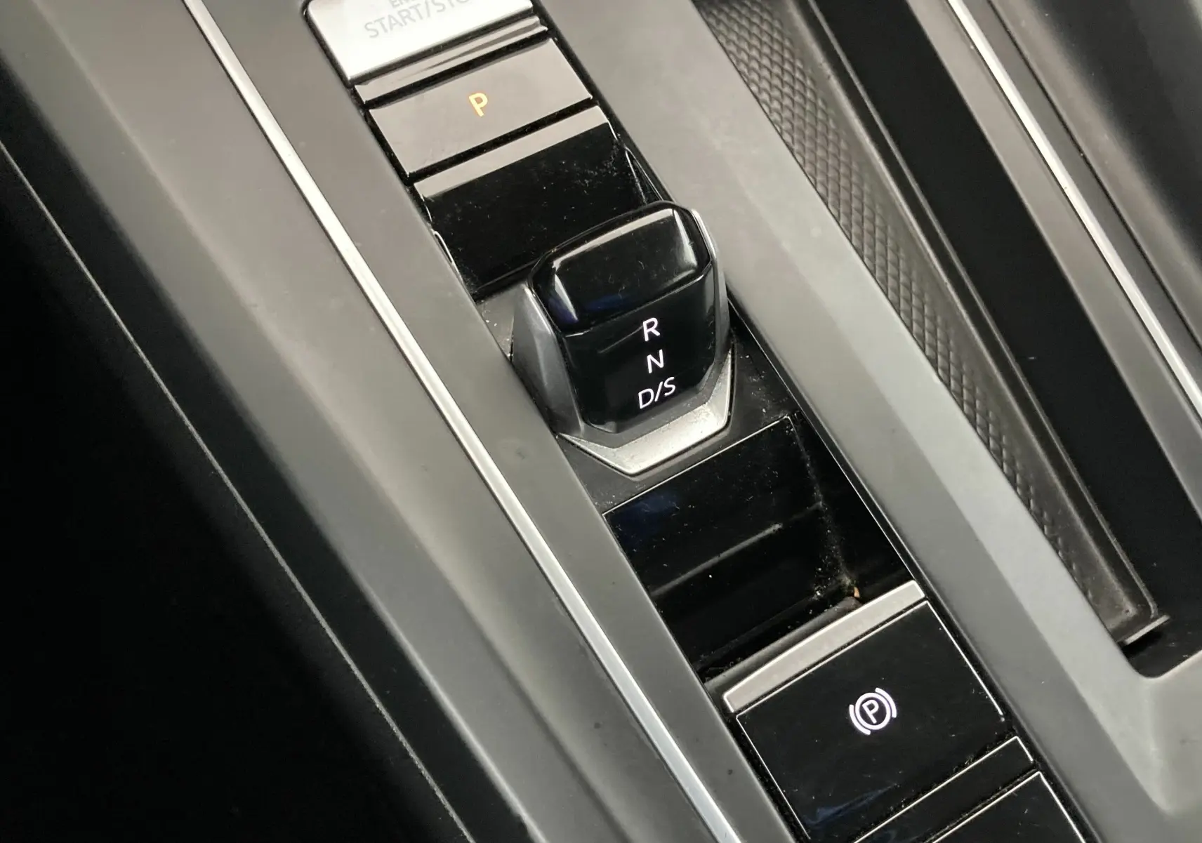 Gros plan sur la commande de boîte automatique noire de la Volkswagen Golf VIII gris reflex, avec bouton de frein à main électronique.