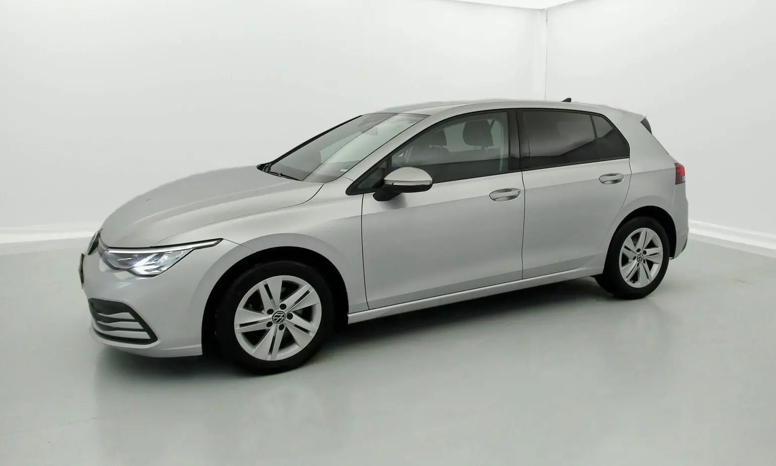 Volkswagen Golf VIII gris reflex vue de profil côté gauche dans un studio lumineux, avec phares allumés.