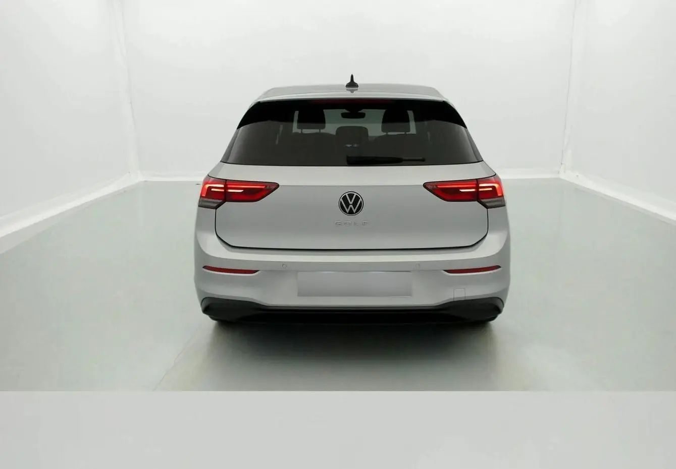 Vue arrière d'une Volkswagen Golf VIII gris reflex avec feux arrière allumés dans un studio blanc.